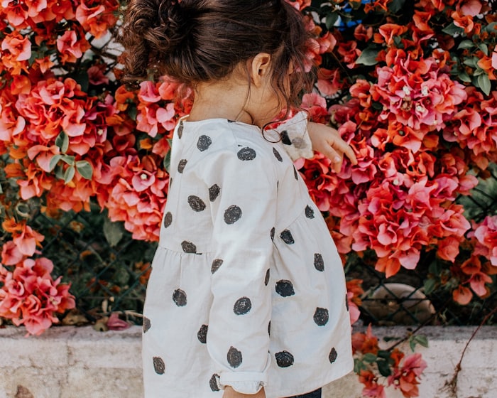 A toddler in a polka-dot top standing by flowers